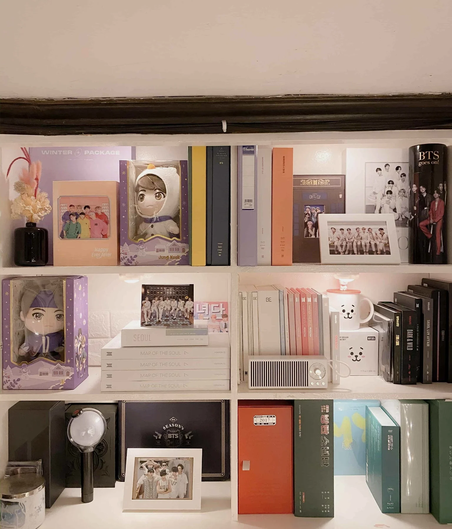 K-pop fan shelf with organized albums, framed photos, and lightstick
